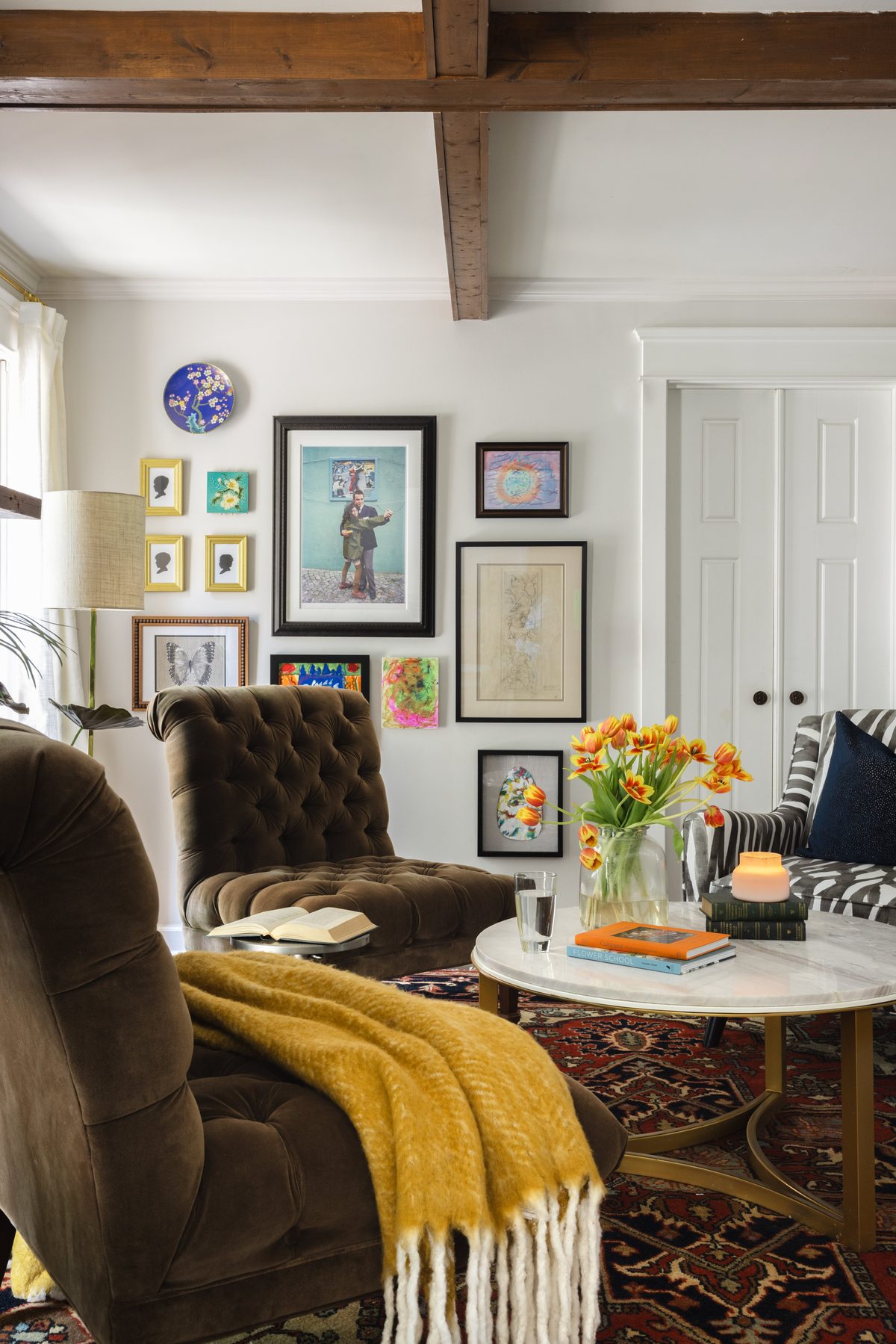 A gallery wall of silhouettes, travel photos, and the kids&rsquo; art above a tufted brown velvet chaise with a mustard mohair throw
