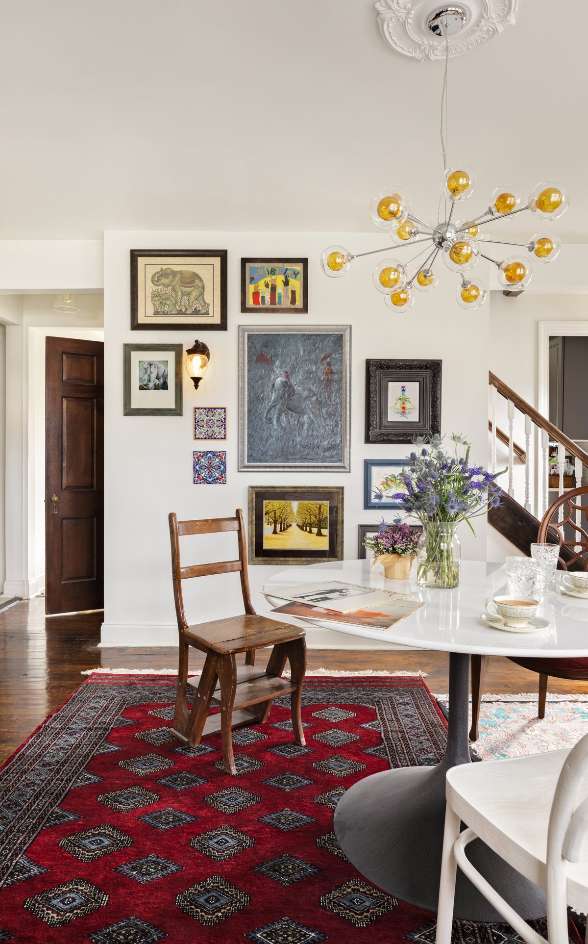 A gallery wall of elephant artwork, Turkish tiles, and collected paintings beside the sputnik chandelier and the tulip table with fresh thistle