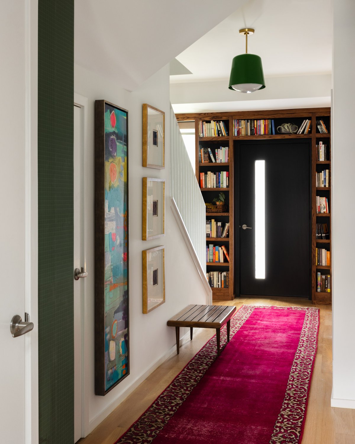 The entry: a black front door framed entirely by built-in walnut bookshelves, with a magenta overdyed runner and a slatted wood bench
