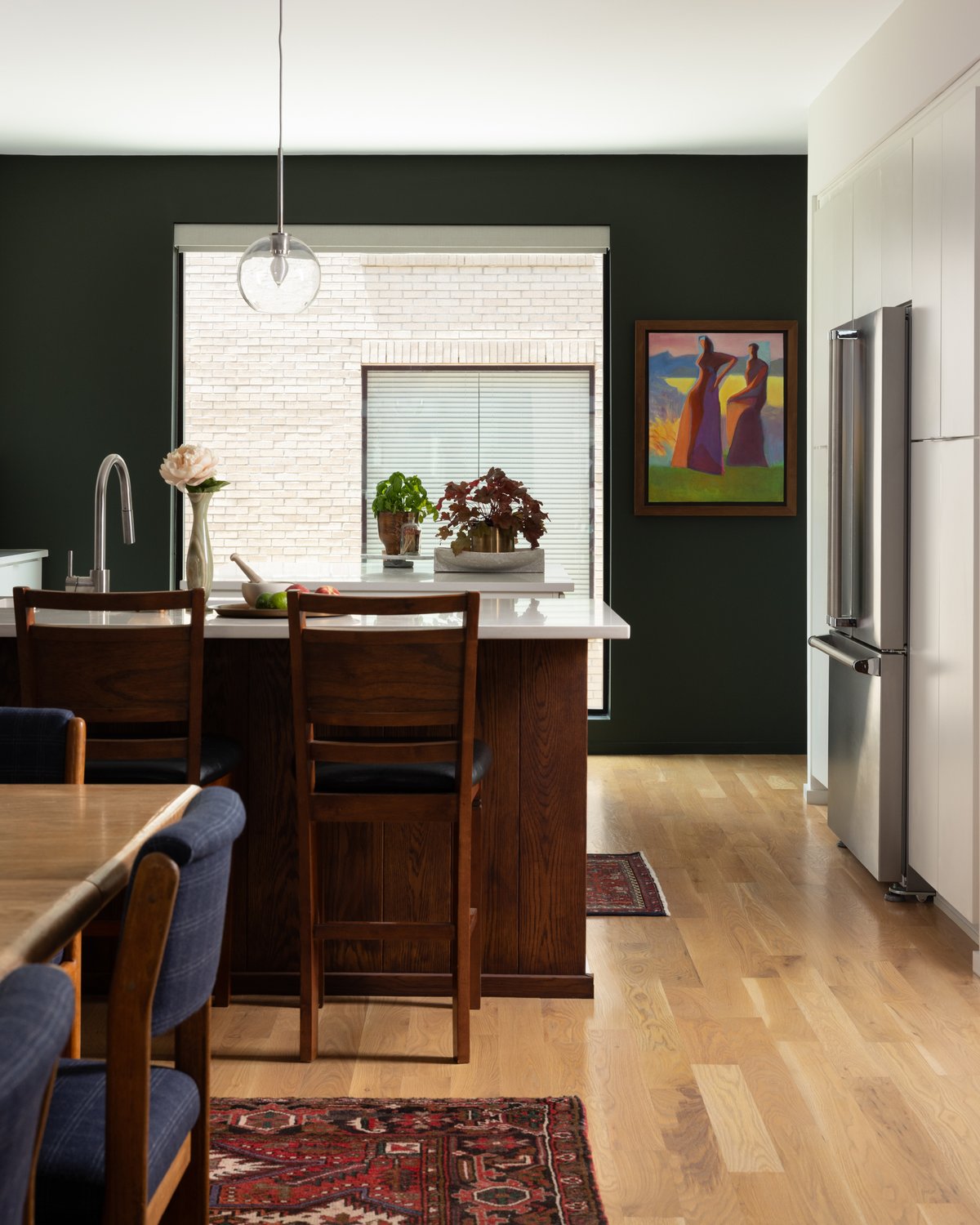 The kitchen: deep green walls, a wood island with white quartz counters, a figurative painting beside the window, and a vintage runner on the floor