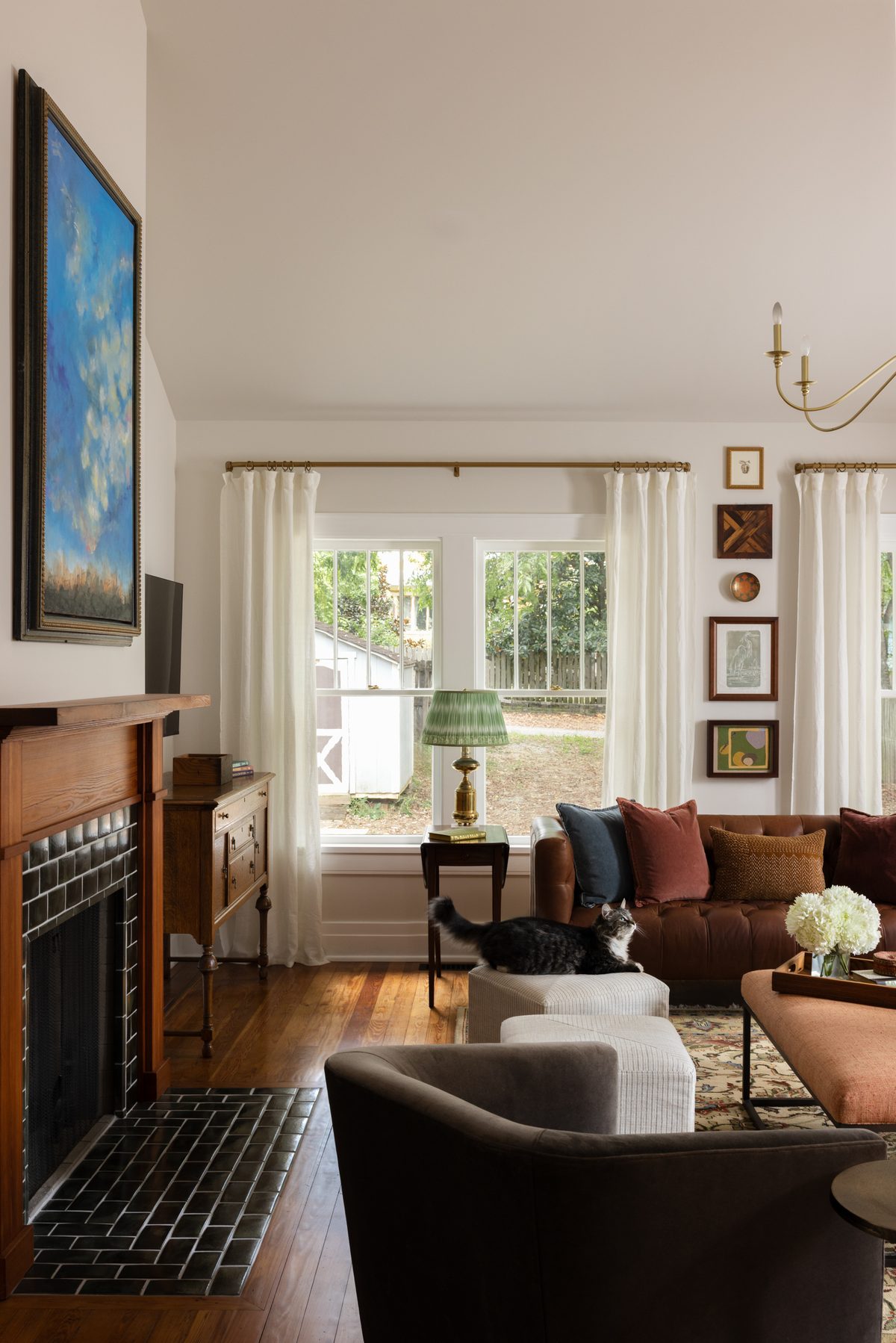 The handmade mantle and dark-green-tiled fireplace beneath a large blue landscape painting, with a brass candle sconce