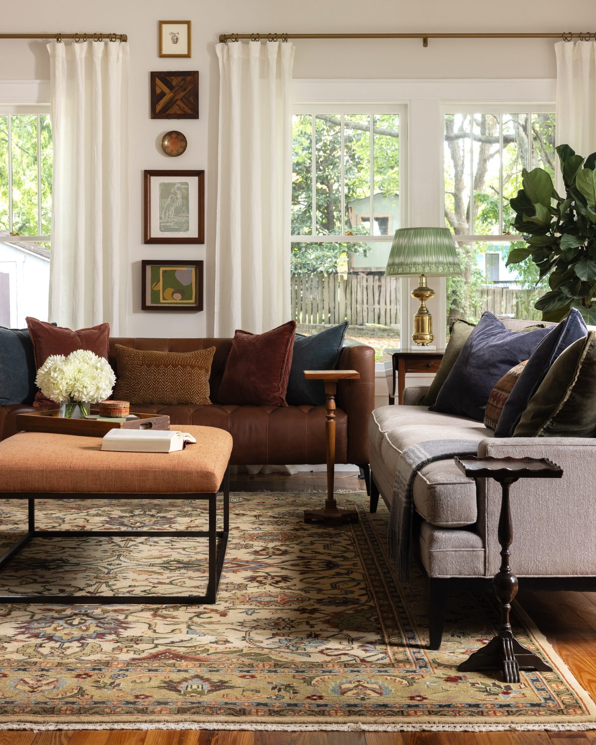 A great room with a tufted leather sofa and an oatmeal sofa around an orange linen ottoman on a vintage rug