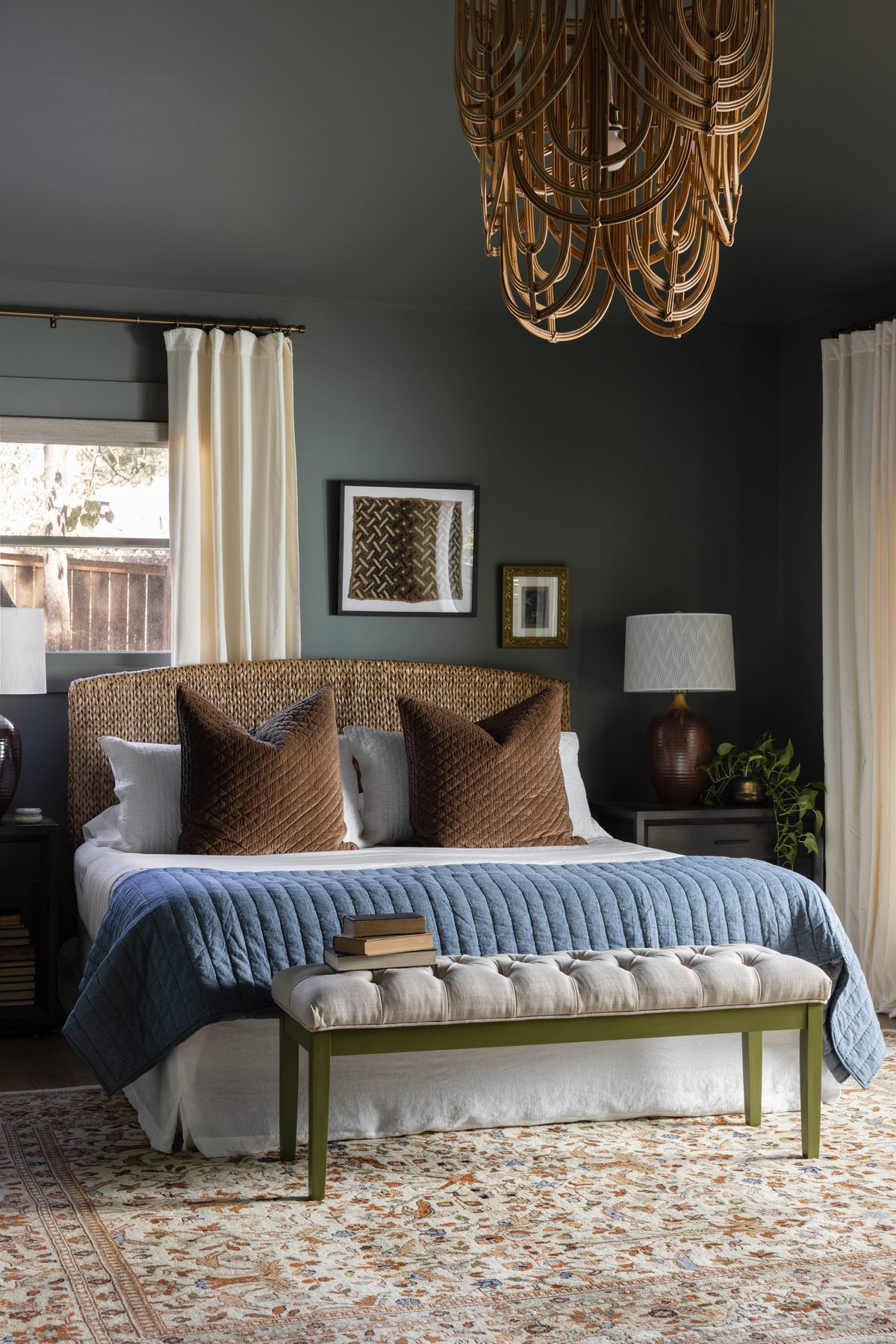 The finished Green Bedroom, straight on: deep green walls and ceiling, a rattan chandelier, the seagrass headboard with brown velvet pillows, a blue quilt, a tufted bench on a green-painted frame, and a vintage rug