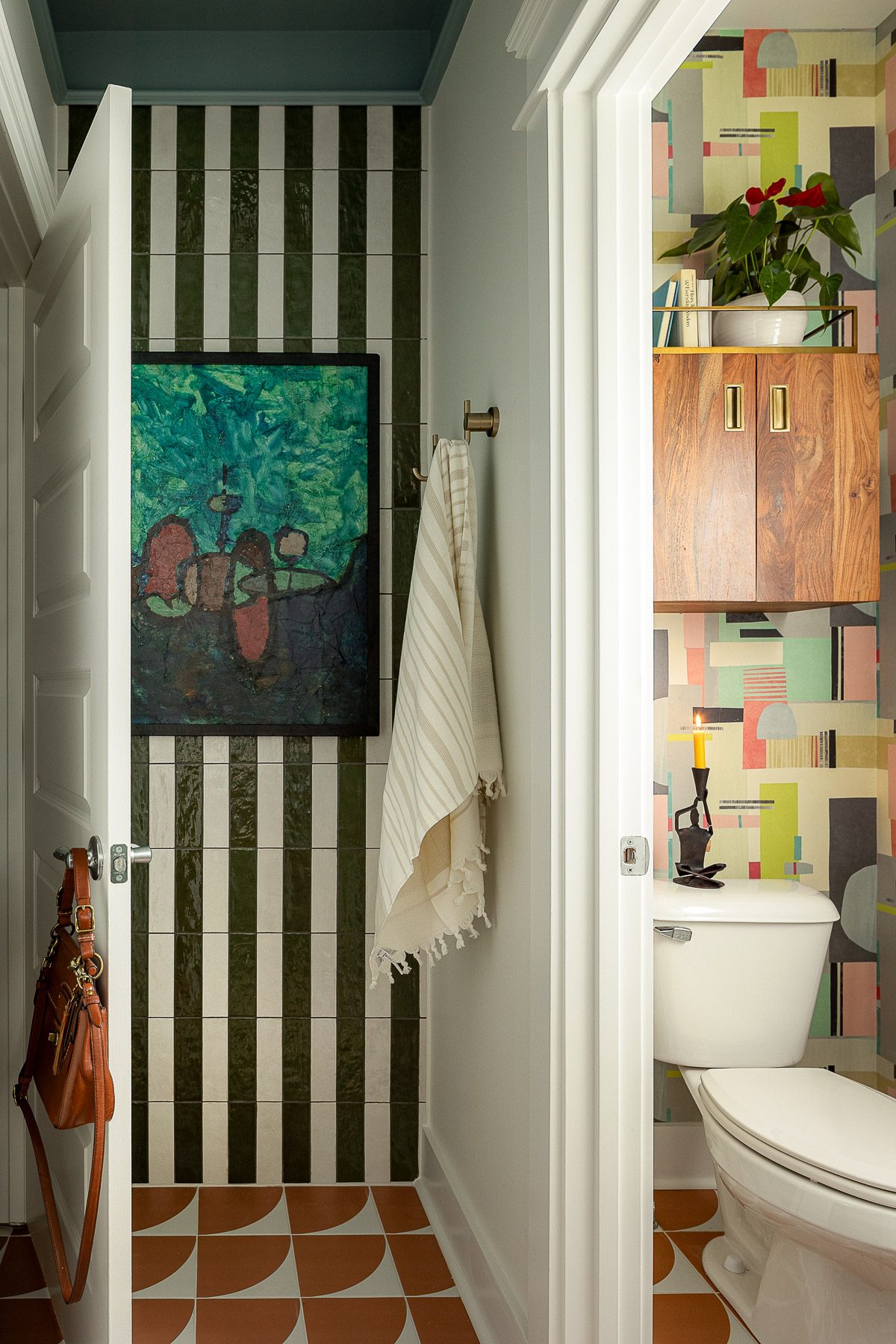 A bathroom doorway with black-and-white striped walls, a vintage painting, and a colorful patchwork tile wall