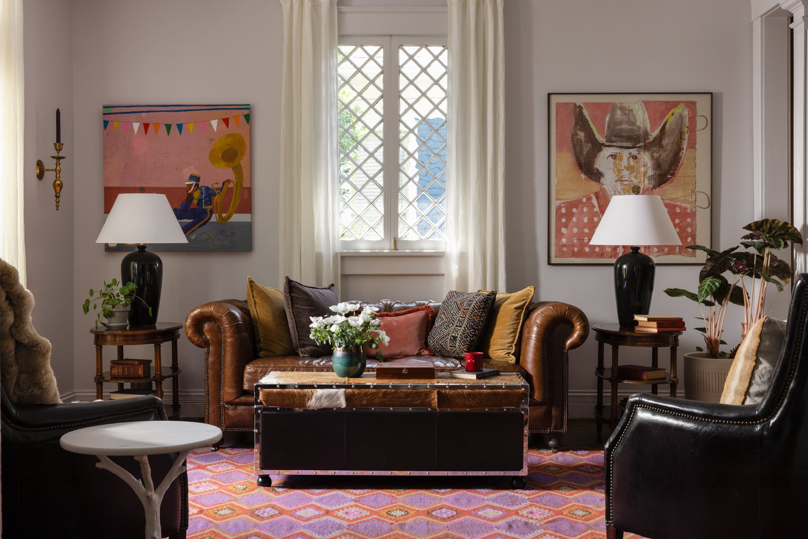A preloved leather Chesterfield sofa layered with velvet and kilim pillows, flanked by lamps and collected art