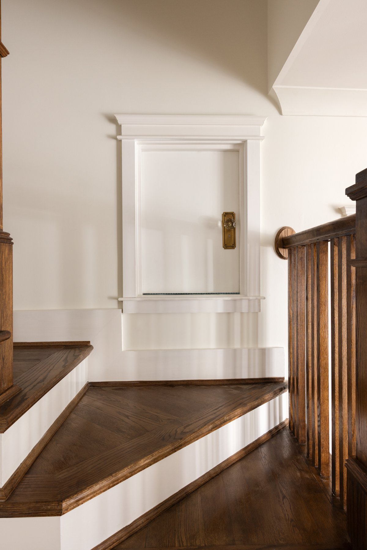 A small white paneled door with an antique glass knob set into the wall at the stair landing, closed