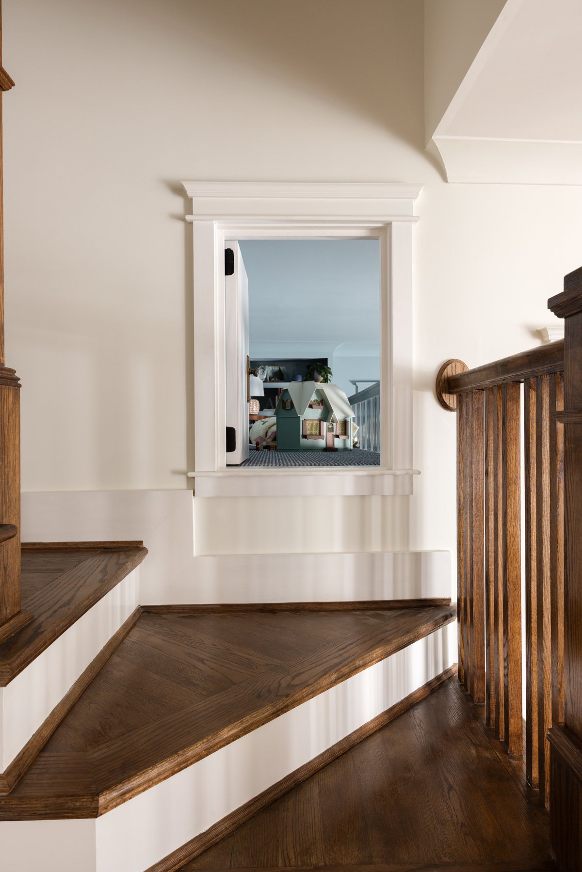 The same little door swung open at the stair landing, revealing the dollhouse and striped carpet of the loft inside
