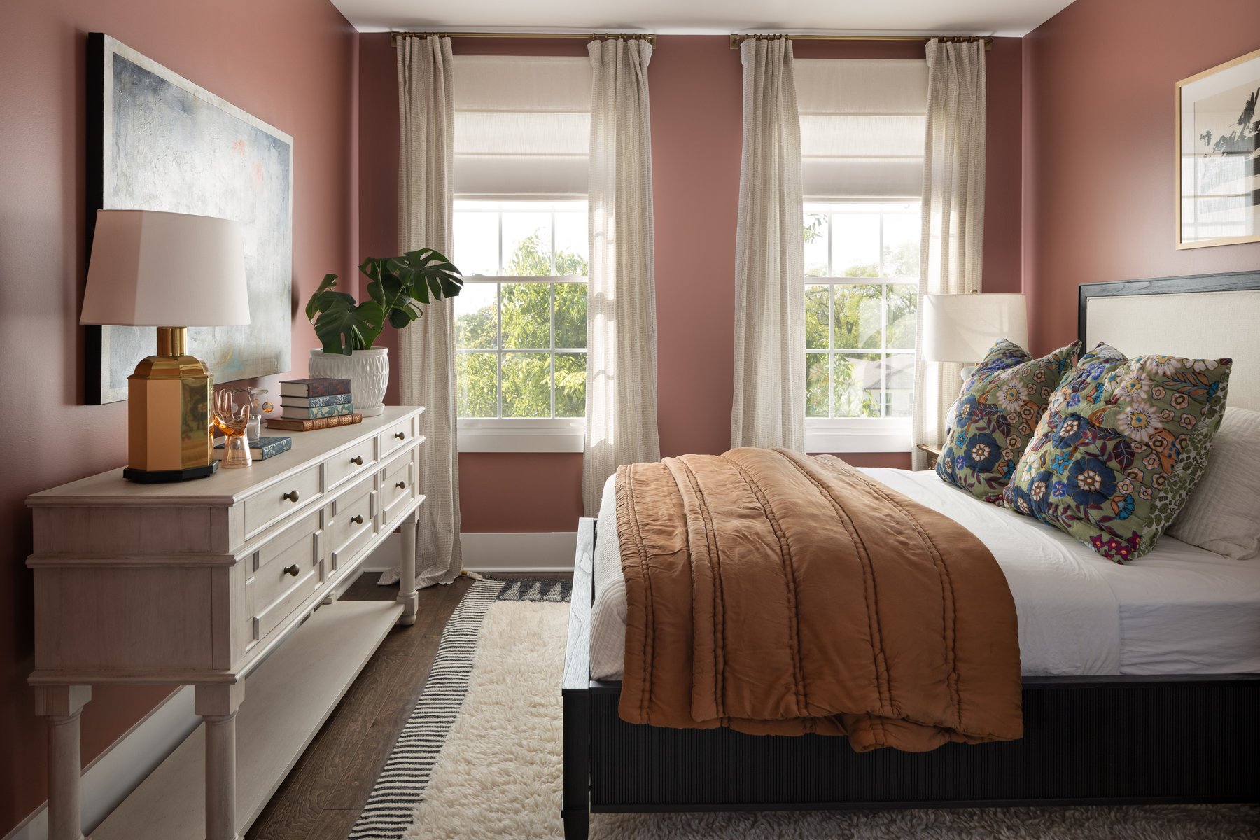 The guest bedroom: pink walls, a black bed with a terracotta quilt and floral pillows, a whitewashed dresser with a brass lamp, and layered rugs
